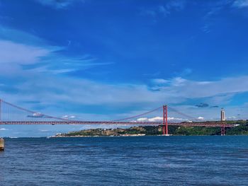 Suspension bridge over river against cloudy sky