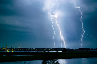 Lightning over illuminated city against sky at night