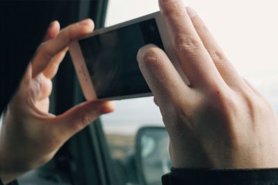 Cropped image of person photographing through mobile phone in car
