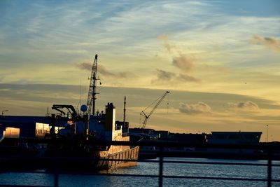 Silhouette of cranes at harbor against cloudy sky during sunset