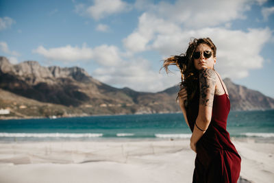 Side view of young woman standing at beach against sky