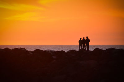 Silhouette people on beach against orange sky