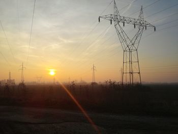 Silhouette electricity pylon on field against sky during sunset