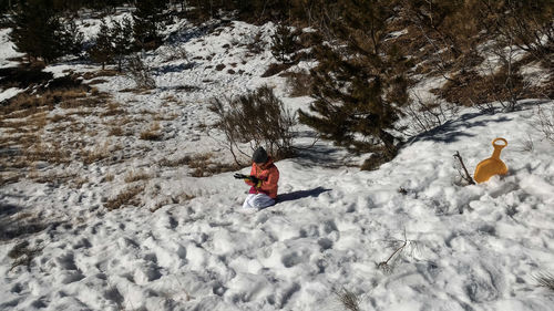 Girl wearing gloves while kneeling on snow during winter