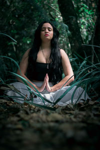 Woman with eyes closed mediating on land in forest