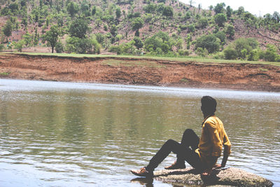 Rear view of men sitting on lake against sky