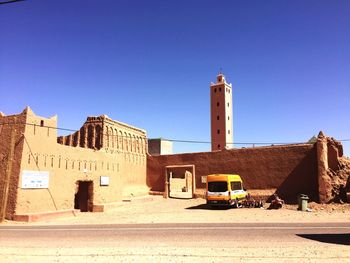 Road amidst buildings against clear blue sky