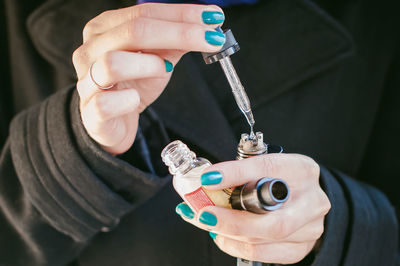 Midsection of woman holding electronic cigarette and dropper