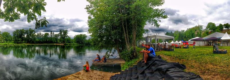 Reflection of people in lake against cloudy sky