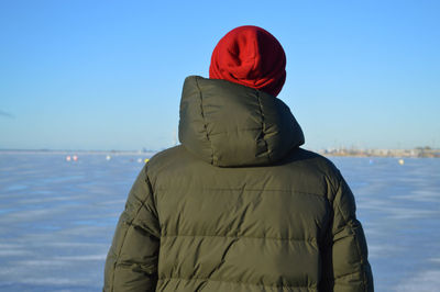 Back view of a man wears green jacket and red hat looking at sea