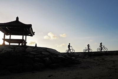 Silhouette people riding bicycle against sky