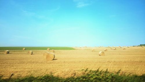 Hay bales on field against clear blue sky