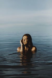 Young woman with mud on face looking away while swimming in lake against sky