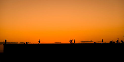 Silhouette people standing against orange sky