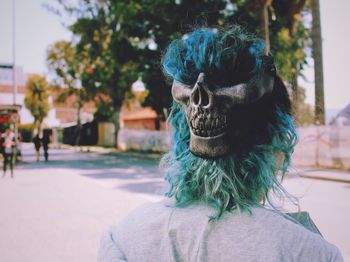 Rear view of person wearing mask by tree on road