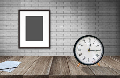 Close-up of clock on wooden table against picture frame molded on wall