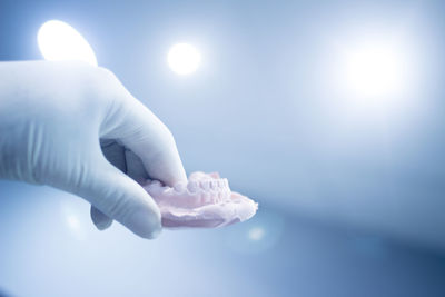 Cropped hand of person holding dental mold against illuminated lights