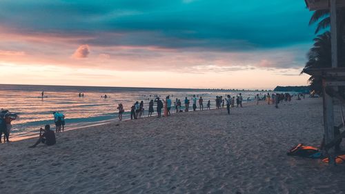 People at beach against cloudy sky during sunset