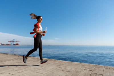 Full length of woman running by railing against sea