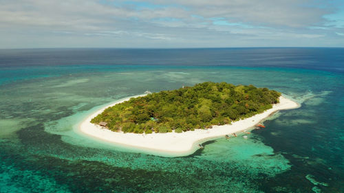 Tropical island and sandy beach surrounded by atoll and coral reef with turquoise water