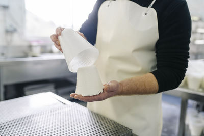 Mature male chef removing cheese from container in factory