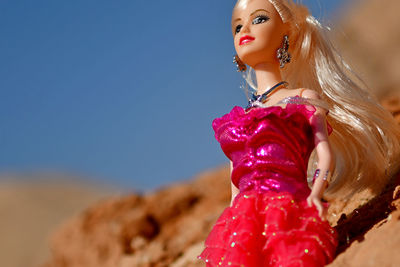 Close-up of pink doll on sand against clear blue sky