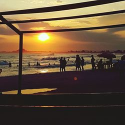 Silhouette people on sea against sky during sunset