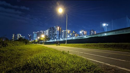 Illuminated street by road against sky at night