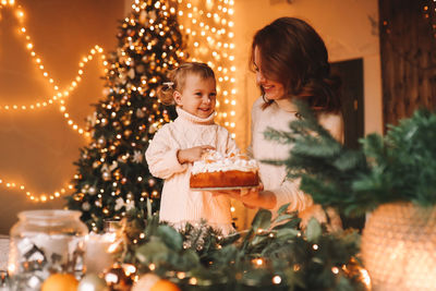 Happy mom and daughter in sweaters together prepare a cake for the christmas holiday in the kitchen