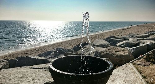 Splashing water fountain at beach against sky