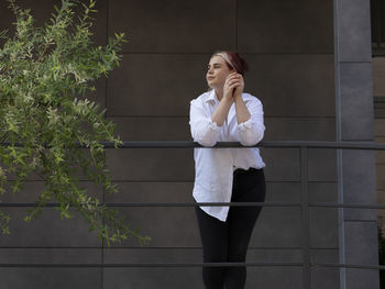 Bottom view high-rise building with tree, young business woman 20s looking around. caucasian