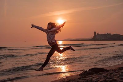 Full length of girl jumping at beach during sunset