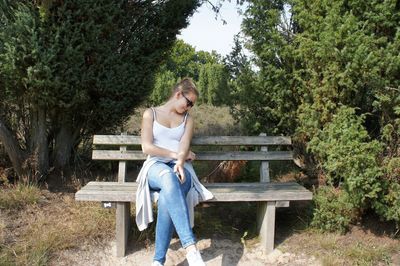 Full length of woman sitting on bench by trees