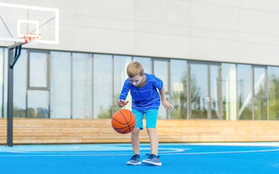 Boy playing with basketball while standing on sports court