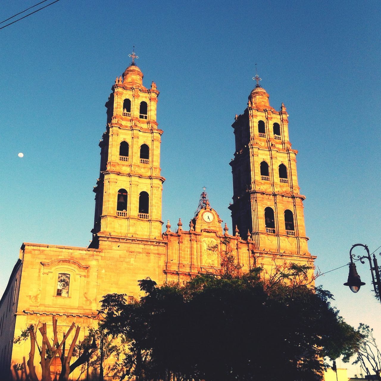 building exterior, architecture, built structure, clear sky, low angle view, religion, place of worship, residential building, building, blue, church, yellow, sunlight, travel, sky, incidental people, outdoors, residential structure, transportation, old town