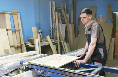 A carpenter cuts wood on a circular saw in a joinery. furniture manufacture.