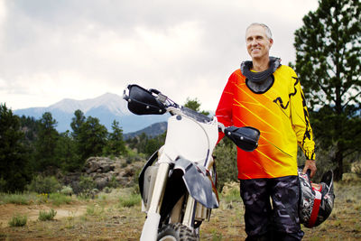 Portrait of man standing by dirt bike against sky