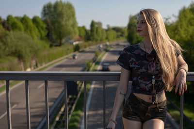 Young woman looking away while standing by railing on footbridge