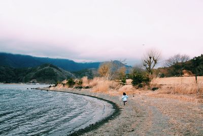 Rear view of girl running on lakeshore against cloudy sky