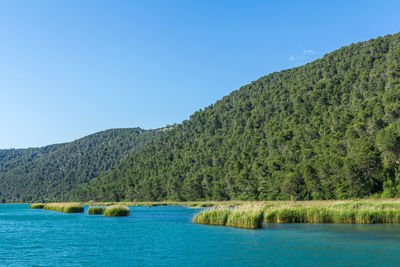 Scenic view of lake and mountains against clear blue sky