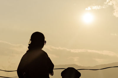 Rear view of silhouette woman standing against sky during sunset