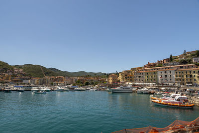 Sailboats moored in harbor by buildings against clear blue sky