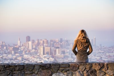 Rear view of woman looking at cityscape against sky