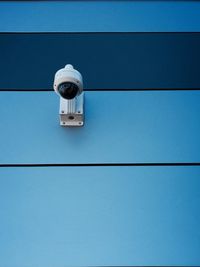 Low angle view of security camera on blue wall