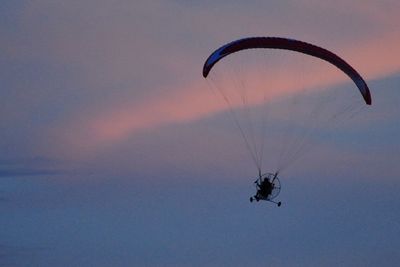 Low angle view of people paragliding against sky during sunset