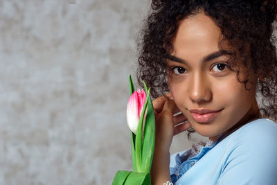 Portrait of beautiful woman holding flower against wall