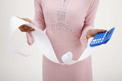 Midsection of woman holding receipt and calculator against white background