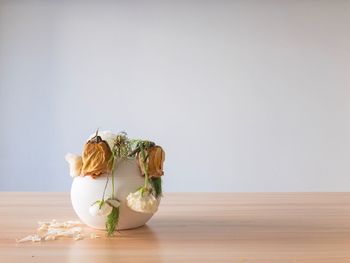 Wilted flowers in vase on table against white wall
