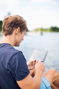 Rear view of mature man using digital tablet at lake