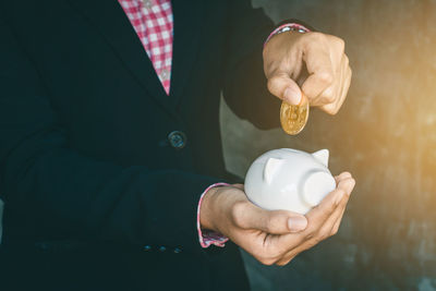 Midsection of businessman putting bitcoin in piggy bank